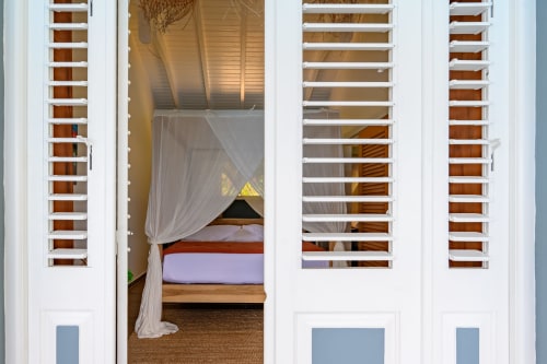 Chambre Touloukaéra chez Marie et Philippe, Marie-Galante : volets ajourés, lit à baldaquin et terrasse avec vue mer