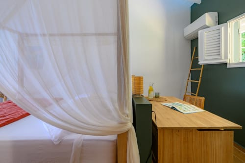 Chambre Touloukaéra chez Marie et Philippe, Marie-Galante : bureau en bois avec climatisation, murs verts, rideaux voilages et