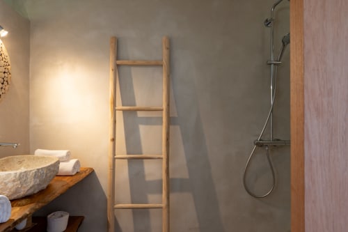 Salle de bain moderne chez Marie et Philippe avec lavabo en pierre, échelle à serviettes en bois et douche pluie à Marie-Galante