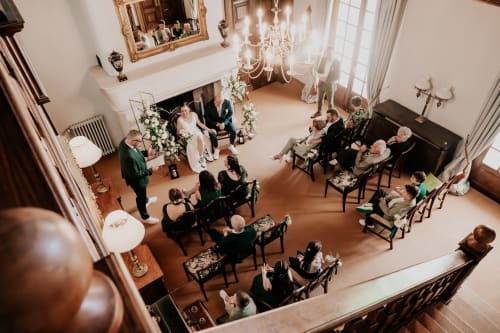Elegante Hochzeitszeremonie in einer prächtigen Manorsaal mit Kronleuchtern, sitzende Gäste, Paar unter Blumenbogen, Domaine de Bize