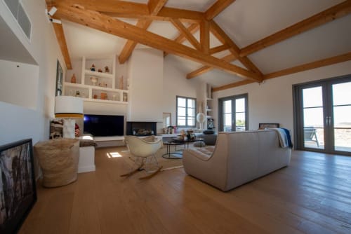 Spacieux salon de villa avec poutres en bois apparent, cheminée, mobilier contemporain, vue sur mer et accès direct à la terrasse