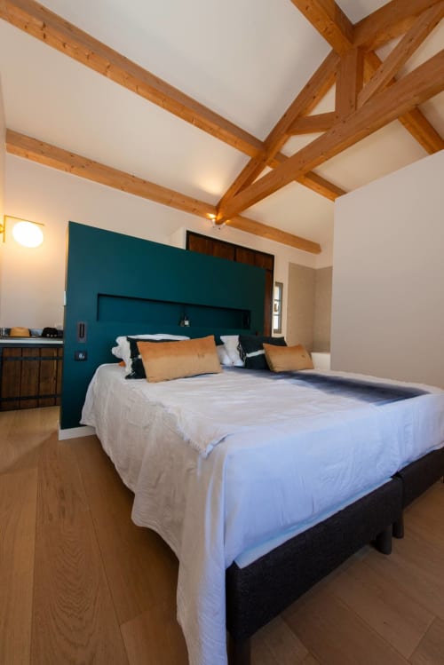 Chambre moderne avec tête de lit bleu-vert, poutres apparentes, linge blanc et coussins dorés à Villa Camille à Centuri