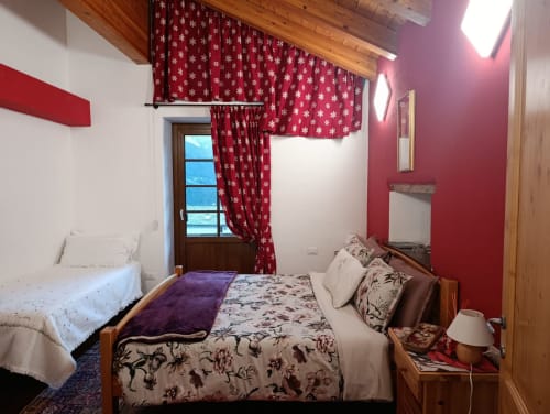 Accogliente camera da letto a La Tour B&B a Oyace con festivi tendaggi rossi a fiocchi di neve, travi di legno, finestra con vista montagna e dettagli floreali