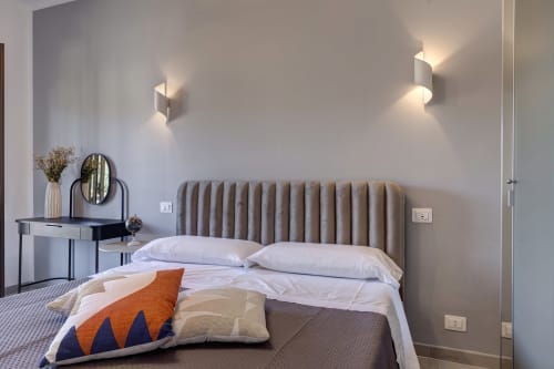 Modern double bedroom at Palazzo Belvedere with taupe quilted headboard, white bedding, desk, wall sconces, and contemporary