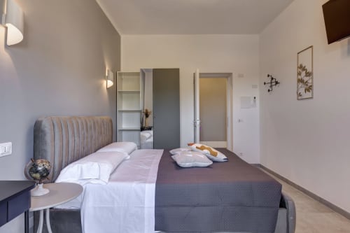 Modern double bedroom at Palazzo Belvedere hotel with grey upholstered bed, white linens, minimalist decor, and tile flooring