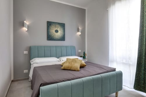 Modern double bedroom at Palazzo Belvedere with teal upholstered bed, gray bedding, decorative pillows, wall sconces, and