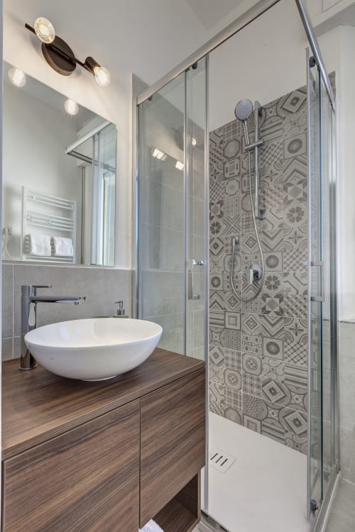 Modern bathroom at Palazzo Belvedere with white vessel sink, wood vanity, patterned shower tiles, and glass enclosure