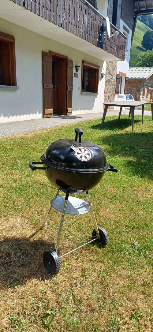 Barbecue kettle noir sur l'herbe au Chalet Les Arcosses, La Giettaz avec chalet alpin et table à manger en arrière-plan