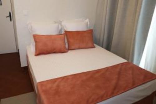 Lit double moderne avec literie blanche, oreillers et jeté de couleur rouille dans une chambre d'hôtel lumineuse à l'Hotel Villa