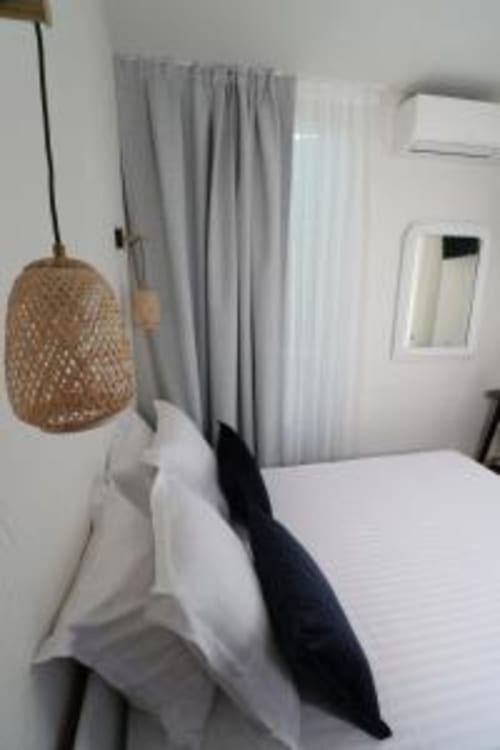 Chambre moderne de l'Hôtel Villa Roseraie avec luminaire suspendu tressé, literie blanche, rideaux gris et climatisation