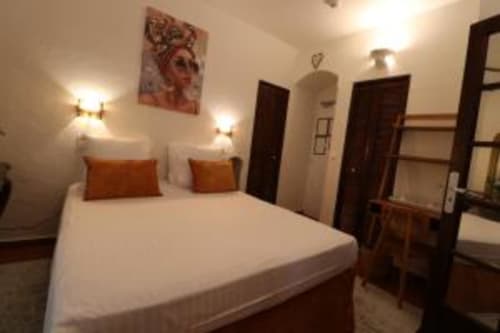 Spacious queen bedroom at Hotel Villa Roseraie in Vence with white bedding, orange cushions, warm lighting, and dark wooden