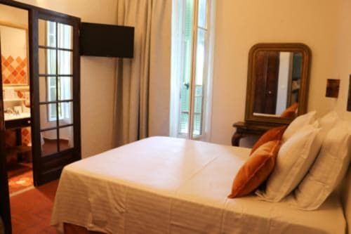 Spacious bedroom at Hotel Villa Roseraie in Vence with queen bed, orange accents, garden view doors, and wooden furnishings