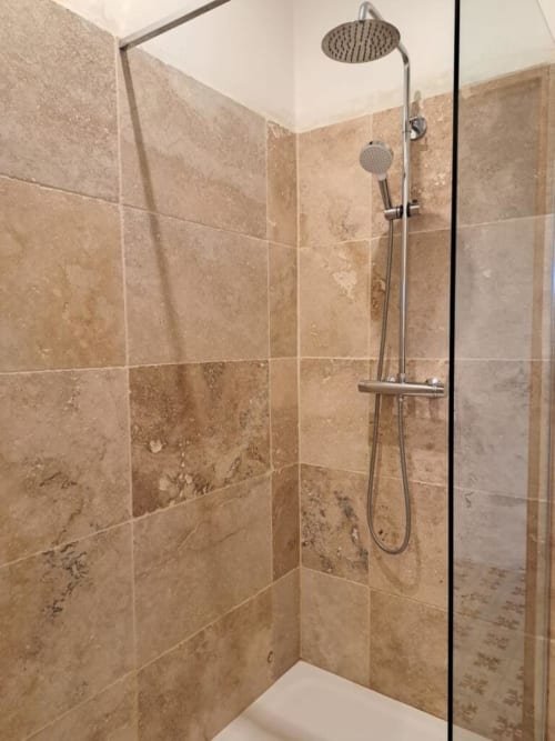 Douche moderne avec carrelage en travertin, pluie de tête et douchette dans le gîte Chez Laure & Marc