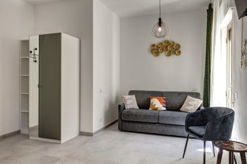 Modern hotel room at Palazzo Belvedere with gray sofa, wardrobe, pendant light, and balcony access in Chianciano Terme