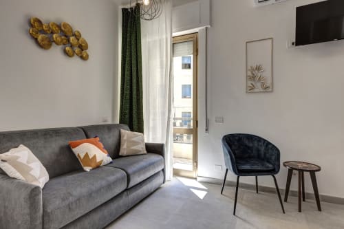 Modern hotel room at Palazzo Belvedere with gray sofa, black velvet chair, golden wall art, and balcony at Chianciano Terme