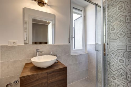 Modern bathroom at Palazzo Belvedere with white vessel sink, wood vanity, gray tiles, and patterned shower enclosure