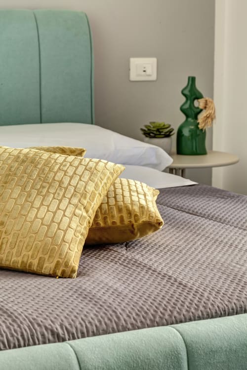 Elegant double bedroom at Palazzo Belvedere with gold pillows, gray bedding, mint headboard, and modern décor in Chianciano