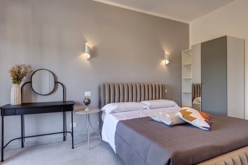 Modern double bedroom at Palazzo Belvedere with upholstered headboard, desk, round mirror, and tile flooring