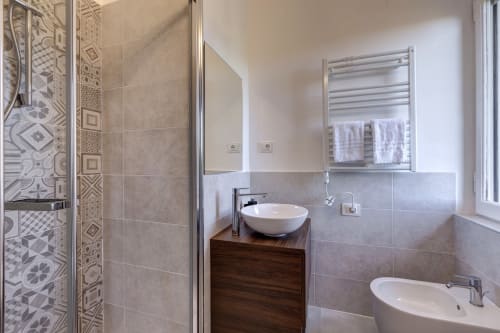 Modern bathroom at Palazzo Belvedere hotel with dual sinks, heated towel rack, and decorative patterned shower enclosure