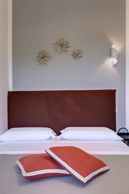 Modern double bed with burgundy headboard, white pillows, and red decorative cushions at Palazzo Belvedere in Chianciano