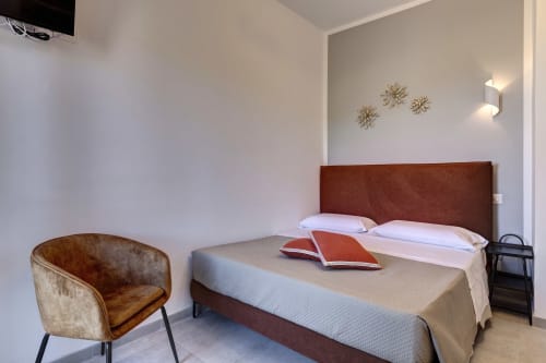 Modern double bedroom at Palazzo Belvedere hotel with terracotta headboard, accent chair, and decorative wall art in