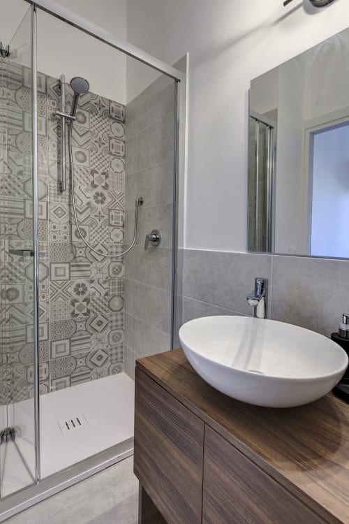 Modern bathroom at Palazzo Belvedere with white vessel sink, patterned tile shower, glass enclosure, and wooden vanity