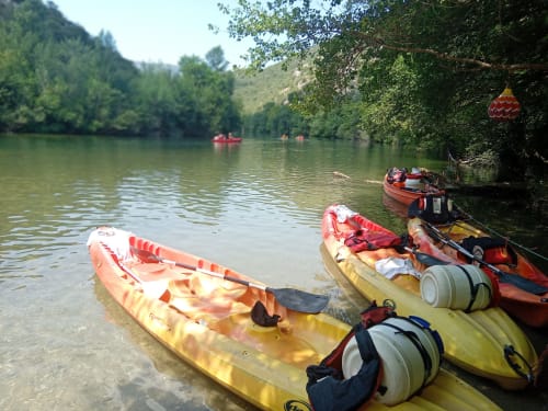 Kayaks alignés sur la berge près de Chez Laure & Marc, Plaissan, France, avec une végétation luxuriante et des collines