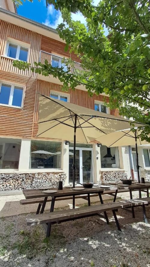 Maison de Sophie BnB patio with wooden picnic tables, large umbrellas, and lush greenery in Rencurel