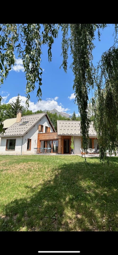 Villa Locavilla à Colombes avec vue sur les montagnes, façade en pierre blanche, toit en métal, saule pleureur, pelouse impeccable et patio
