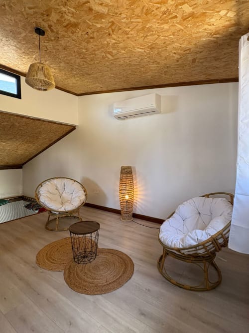 Salon cozy de la villa Au pied des Sources à Cilaos, avec fauteuils en rotin, tapis tissés et plafond en liège