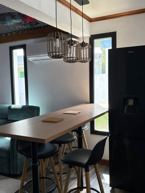 Salle à manger de villa moderne à Au pied des Sources à Cilaos avec table en bois, chaises noires, suspensions et vue sur les montagnes