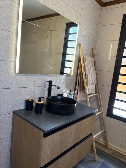Salle de bains moderne avec vasque ronde noire, meuble en bois et miroir illuminé à la villa Au pied des Sources à Cilaos