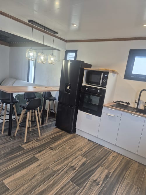 Cuisine et salle à manger modernes avec électroménagers noirs, parquet et luminaires suspendus à Au pied des Sources