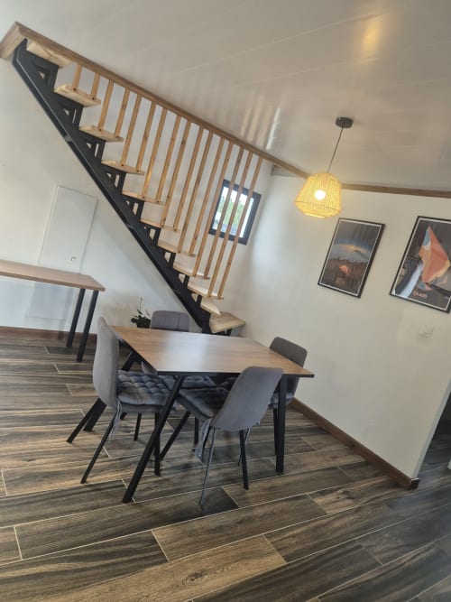 Salle à manger contemporaine avec table en bois, chaises grises et escalier à la villa Au pied des Sources à Cilaos
