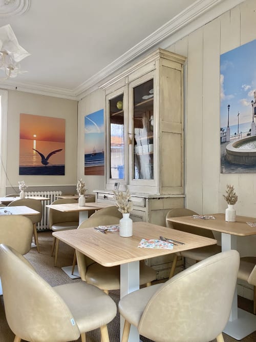 Elegant dining room at Hôtel Maison Richet with cream chairs, wooden tables, coastal artwork, and vintage cabinetry in Les
