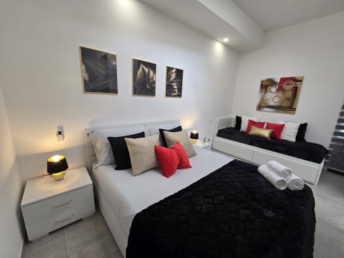 Moderna spavaća soba u apartmanu Raymihome Turin s bijelim krevetom, crvenim akcentima, crnom noćnom lampom, zidnom umjetnošću i drugim krevetom
