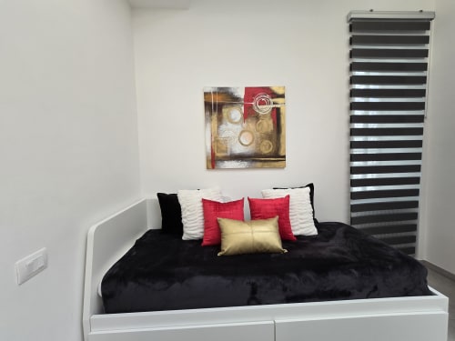 Moderna spavaća soba u apartmanu Raymihome Torino s crnim krevetom, crvenim i zlatnim jastucima, apstraktnom zidnom umjetnosti i prugastim pregradama