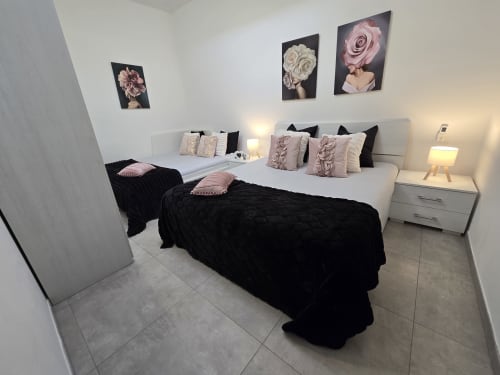 Camera da letto moderna nell'appartamento Raymihome Torino con due letti, arredamento rosa e nero, arte murale floreale e mobili eleganti