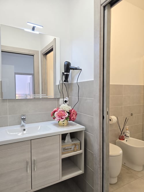 Moderna kupaonica u apartmanu Raymihome u Torinu sa bijelim umivaorom, zrcalom, ružičastim cvijećem i WC-om s pločicama