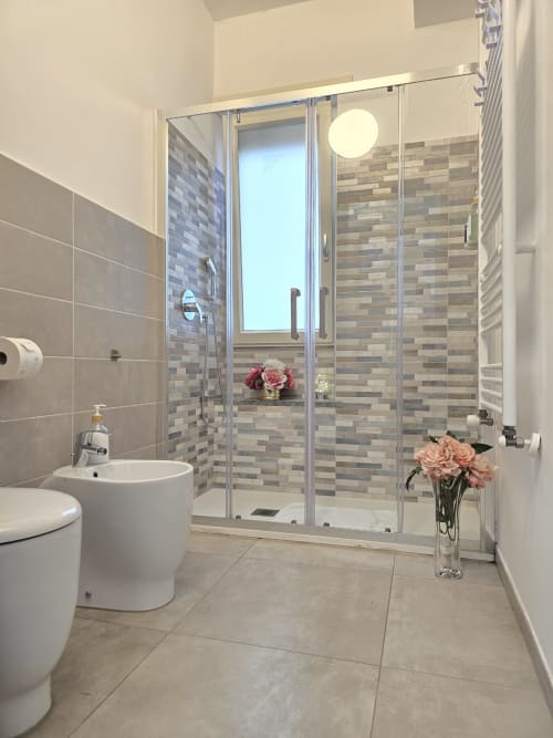 Moderno kupatilo u Raymihome Turin apartmanu sa tuš kabinom, belim toaletom, pedestalni sudopera i svežim cvećem