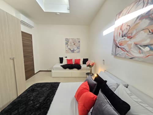 Camera da letto moderna nell'appartamento Raymihome a Torino con letto bianco, cuscini rossi e neri, lucernario e opera d'arte astratta