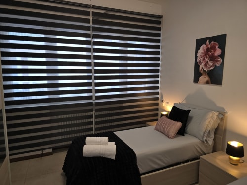 Moderna spavaća soba u apartmanu Raymihome Torino sa prugastim roletama, krevetom sa jastucima i slikom s ružičastim cvećem na zidu