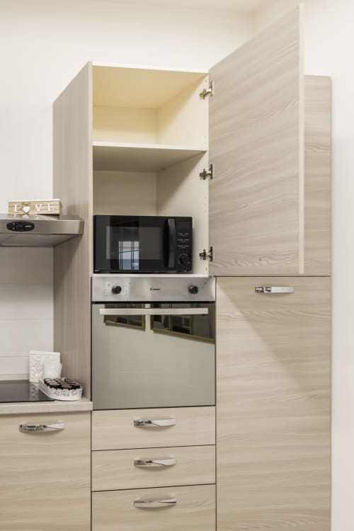 Moderna kuhinja s ormarima od svjetle kreme boje, mikrovalne pećnice, pećnice i otvorenih polica u apartmanu Raymihome u Torinu