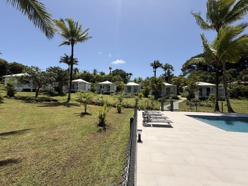 Domaine de la Glacière à Petit Bourg : chaises longues au bord de la piscine, jardins tropicaux et bungalows blancs