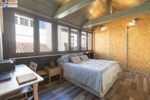 Habitación Penthouse Gracia en CTH Granada con cama queen, paredes de corcho, vigas de madera, escritorio y vistas a la ciudad desde las ventanas