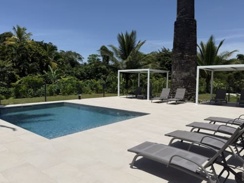 Terrasse de piscine moderne avec transats, pergolas blanches et jardins tropicaux luxuriants au Domaine de la Glacière, Petit-Bourg
