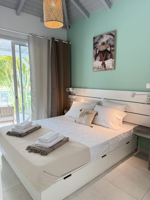 Chambre moderne au Domaine de la Glacière avec mur d'accent vert menthe, lit blanc et vue tropicale sur le balcon à Petit