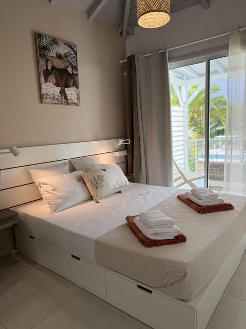 Chambre moderne et lumineuse à la Domaine de la Glacière en Guadeloupe avec lit blanc, balcon vue mer et décor tropical