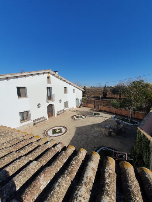 Masía blanca rural con patio, tejas de barro y vistas al campo cerca de Barcelona
