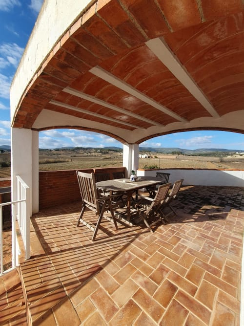 Terraza cubierta en Masía Rural Ca l'Eloi Janet cerca de Barcelona, con mesa de comedor, vigas de madera y vistas al campo